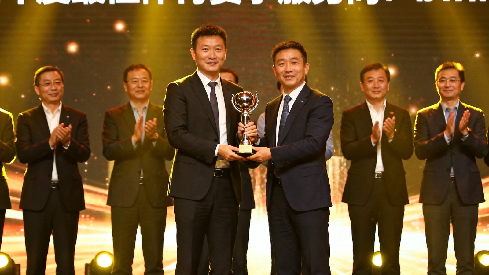 bwin代表在长三角体育产业峰会颁奖典礼上接过年度最佳体育赛事服务商的奖杯，舞台灯光璀璨，背景大屏幕显示获奖企业名单，现场嘉宾鼓掌祝贺。